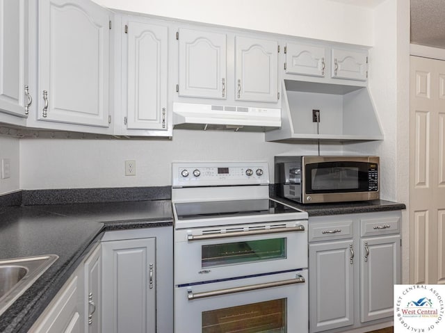 kitchen featuring dark countertops, double oven range, under cabinet range hood, white cabinetry, and stainless steel microwave