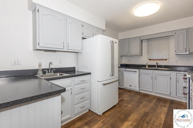 kitchen with dark countertops, dark wood finished floors, white appliances, and a sink