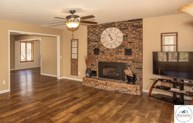 living area featuring baseboards, a textured ceiling, a brick fireplace, and wood finished floors