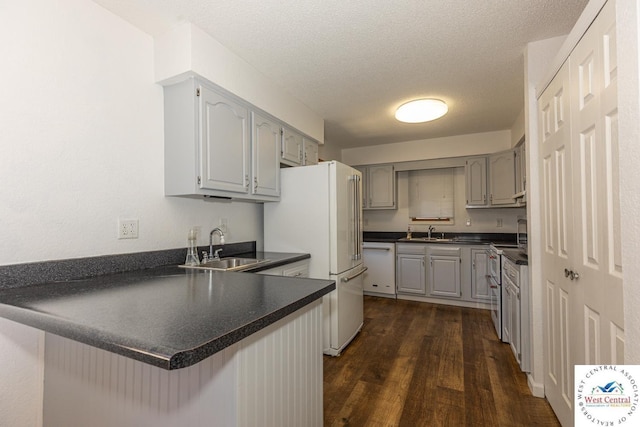 kitchen featuring a sink, white appliances, dark countertops, and a peninsula