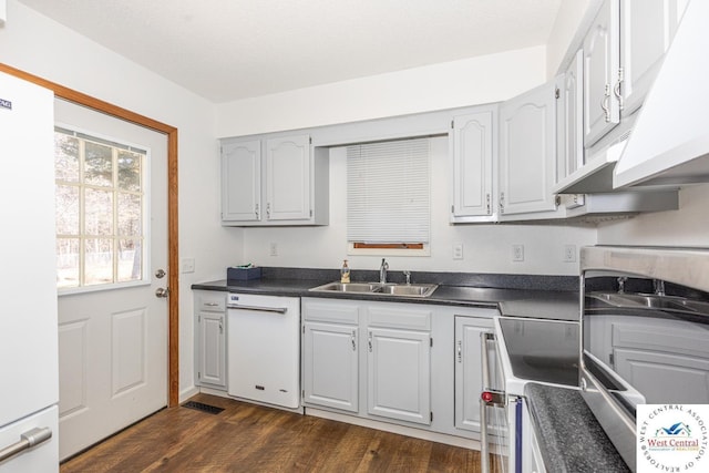 kitchen featuring visible vents, a sink, dark countertops, dark wood-style floors, and white appliances