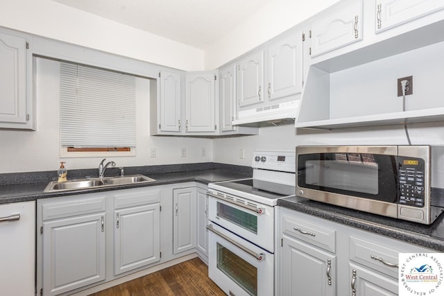 kitchen featuring dark countertops, dark wood-type flooring, under cabinet range hood, white appliances, and a sink