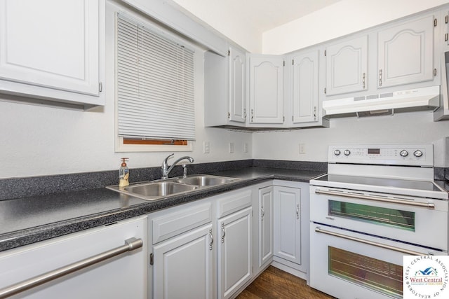 kitchen featuring under cabinet range hood, a sink, dark countertops, dark wood finished floors, and white appliances