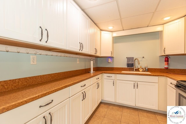 kitchen with a sink, a drop ceiling, white cabinetry, recessed lighting, and light tile patterned floors