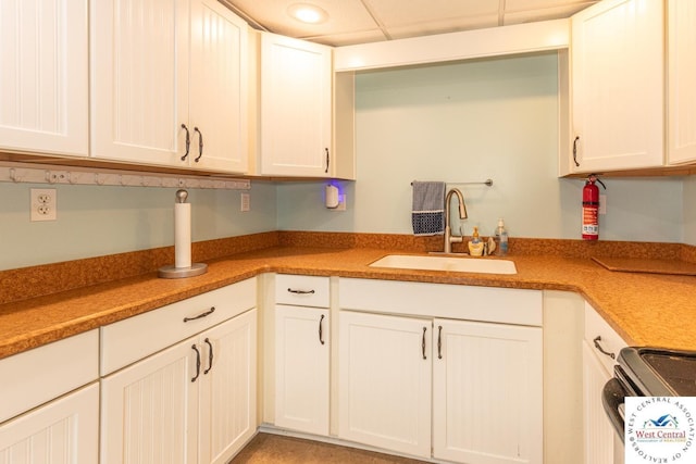 kitchen featuring a drop ceiling, recessed lighting, range with electric stovetop, white cabinets, and a sink