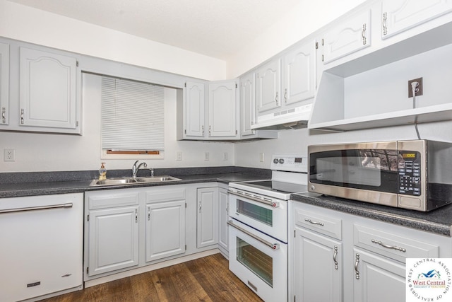 kitchen featuring under cabinet range hood, a sink, dark countertops, dark wood finished floors, and white appliances