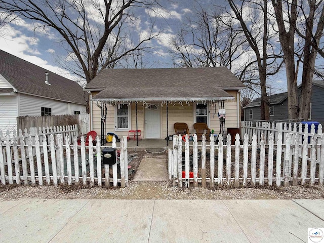 bungalow-style home featuring a fenced front yard, covered porch, and a shingled roof