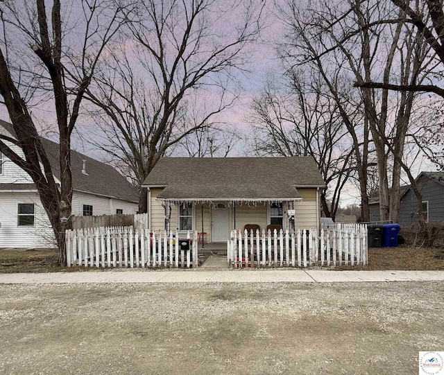 bungalow-style home featuring a fenced front yard and a shingled roof