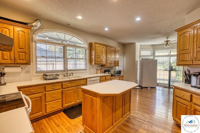 kitchen with brown cabinetry, light wood-style flooring, a center island, light countertops, and a sink