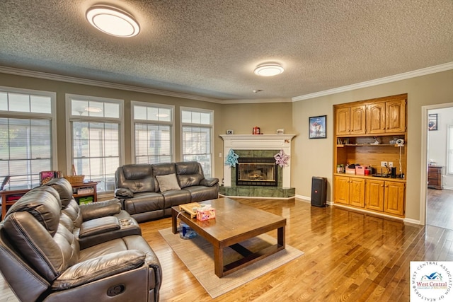 living room featuring light wood finished floors, baseboards, a tiled fireplace, ornamental molding, and a textured ceiling