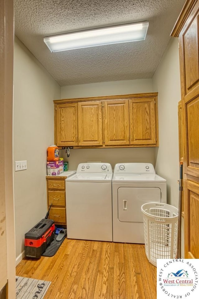 laundry area with light wood-type flooring, washer and dryer, cabinet space, and a textured ceiling