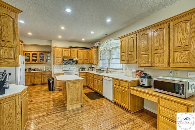 kitchen with white appliances, glass insert cabinets, a center island, light countertops, and a sink