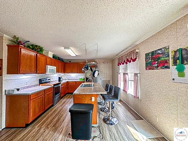 kitchen featuring a kitchen island with sink, light countertops, white microwave, and stainless steel electric stove