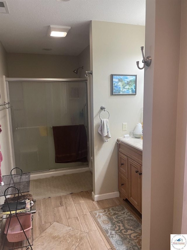 bathroom featuring visible vents, a textured ceiling, wood finished floors, a shower stall, and vanity