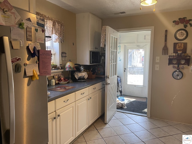 kitchen with light tile patterned floors, visible vents, freestanding refrigerator, a textured ceiling, and dark countertops