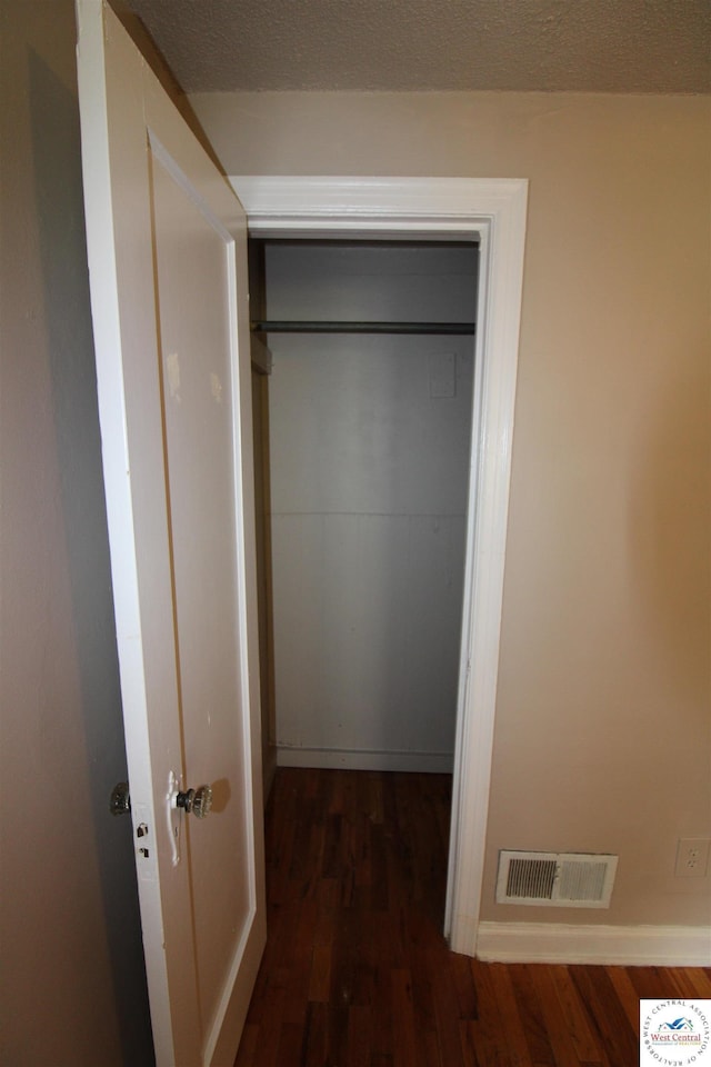 corridor featuring dark wood-type flooring, visible vents, a textured ceiling, and baseboards