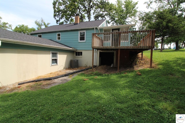 back of property with a shingled roof, a wooden deck, central AC unit, a chimney, and a yard