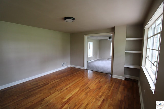 empty room featuring baseboards, visible vents, ceiling fan, wood finished floors, and baseboard heating