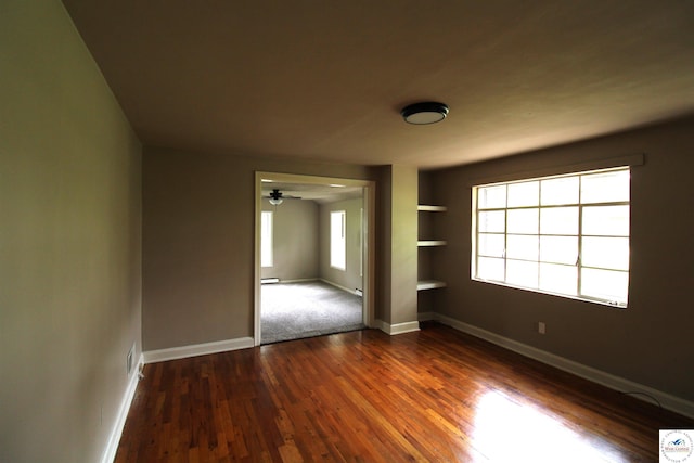 spare room featuring built in shelves, dark wood-style flooring, and baseboards