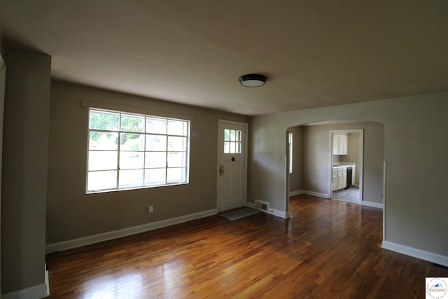 foyer featuring arched walkways, dark wood-style floors, visible vents, and baseboards