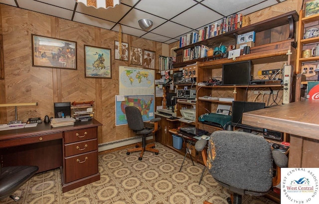 office space featuring a baseboard heating unit, a paneled ceiling, and wood walls