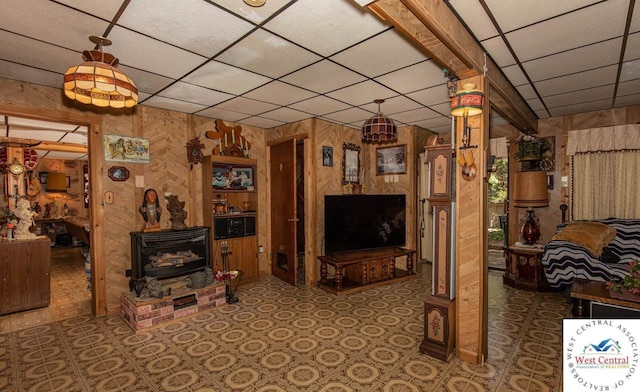 unfurnished living room featuring a wood stove, wooden walls, and a paneled ceiling