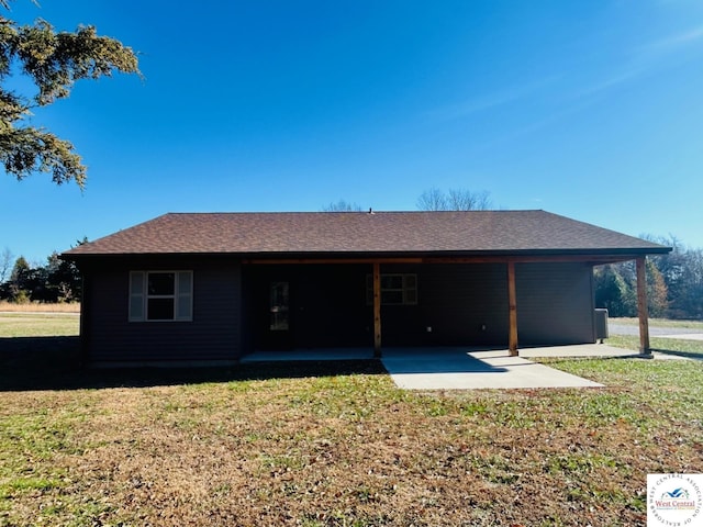 rear view of property featuring a shingled roof and a lawn