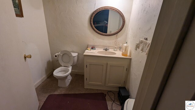 half bath with a textured wall, toilet, vanity, baseboards, and tile patterned floors