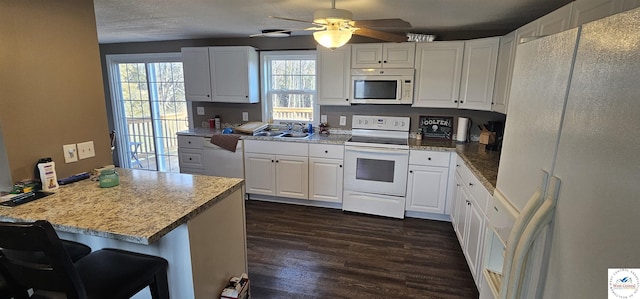 kitchen featuring white appliances, white cabinetry, dark wood finished floors, and a breakfast bar area