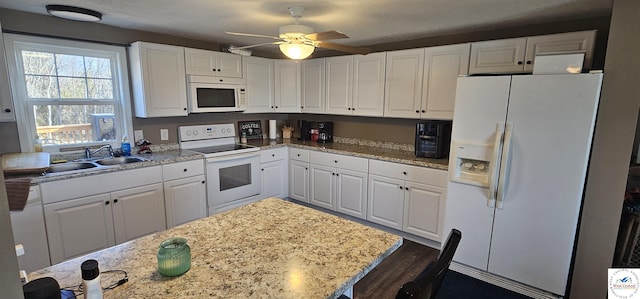 kitchen with white appliances, a sink, a ceiling fan, white cabinets, and light stone countertops