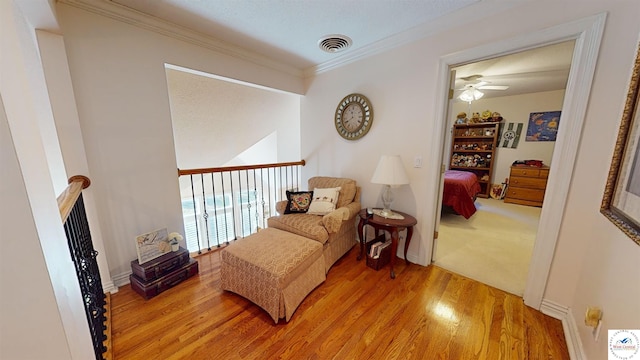 living area featuring light wood-style floors, visible vents, crown molding, and baseboards