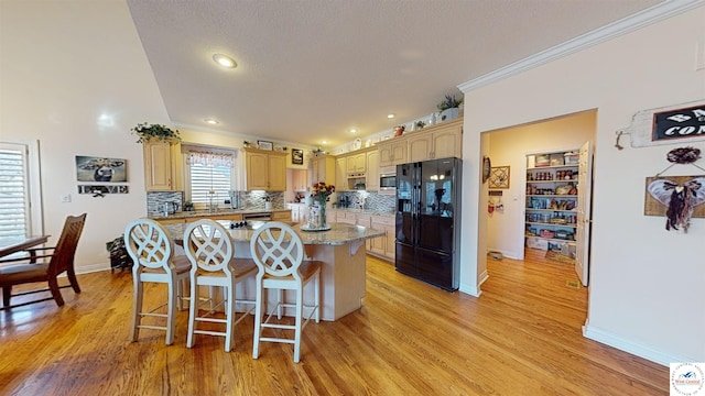 kitchen featuring decorative backsplash, ornamental molding, a center island, light wood-style floors, and black fridge