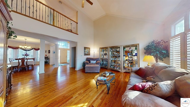 living room featuring high vaulted ceiling, ornamental molding, ornate columns, and wood finished floors