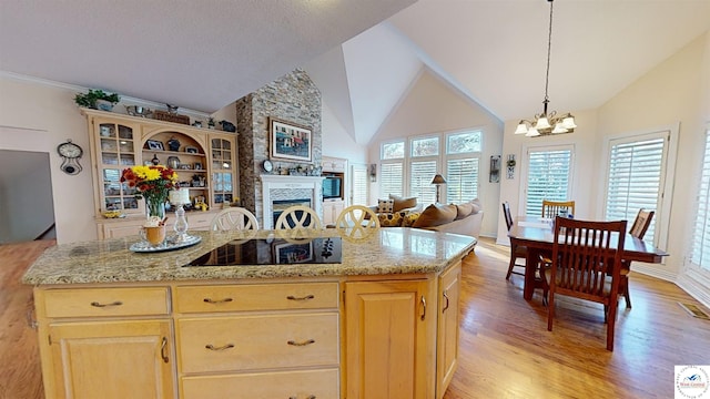 kitchen featuring a large fireplace, open floor plan, a center island, light wood-style floors, and a chandelier