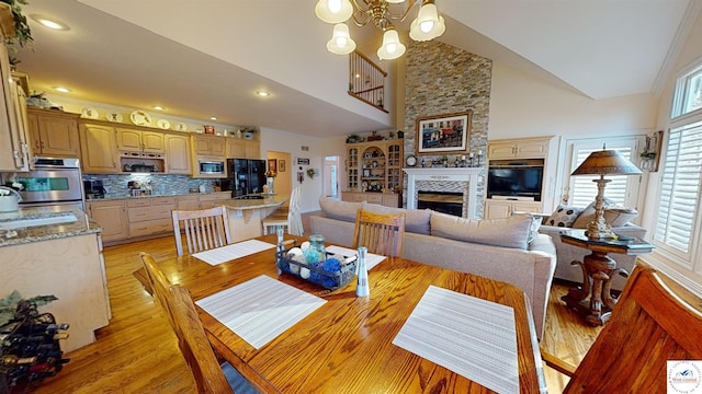 dining space with high vaulted ceiling, light wood-type flooring, a large fireplace, and a notable chandelier