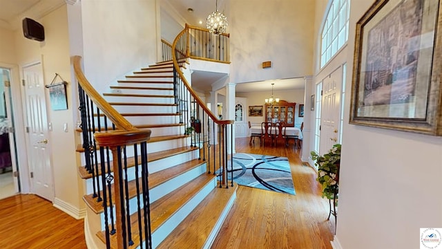 entrance foyer featuring a towering ceiling, an inviting chandelier, wood finished floors, ornate columns, and stairs