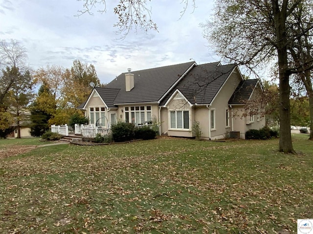 rear view of house featuring a lawn, a chimney, and stucco siding