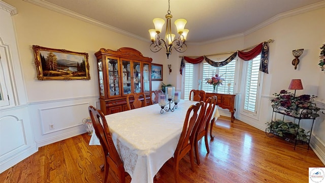 dining room with light wood finished floors, ornamental molding, a wainscoted wall, and an inviting chandelier