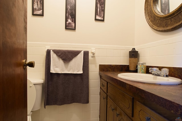 half bathroom featuring toilet, a wainscoted wall, tile walls, and vanity