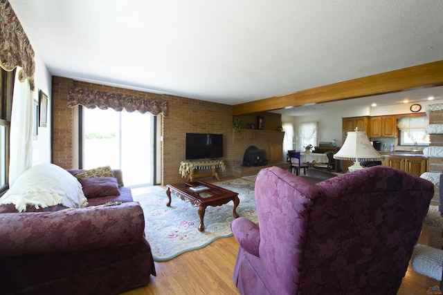 living room featuring light wood finished floors, a brick fireplace, and beam ceiling