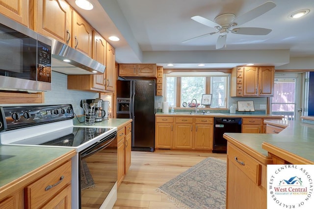 kitchen featuring light wood-style flooring, decorative backsplash, a sink, under cabinet range hood, and black appliances