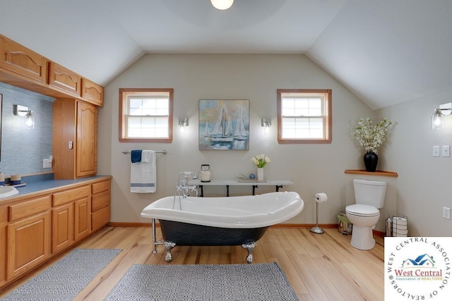 full bathroom with a freestanding tub, baseboards, vaulted ceiling, and wood finished floors