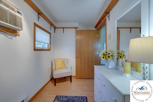 sitting room with light wood finished floors, baseboards, and an AC wall unit