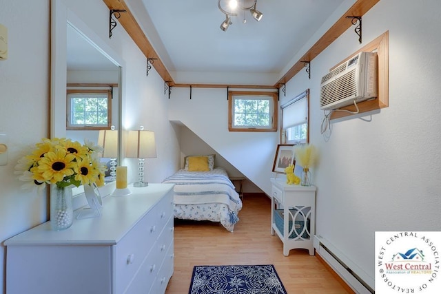 bedroom featuring light wood finished floors, multiple windows, a baseboard radiator, and a wall unit AC