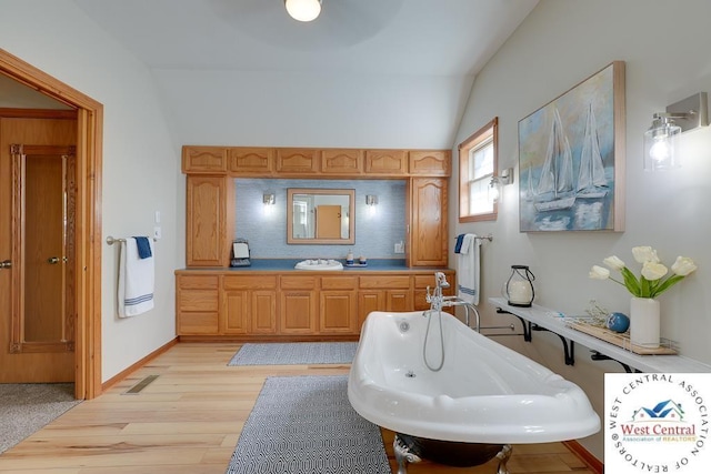 bathroom with lofted ceiling, baseboards, a freestanding bath, and wood finished floors