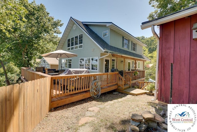 rear view of property with a jacuzzi, a shingled roof, and a wooden deck