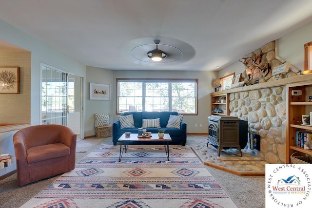 living area with ceiling fan, plenty of natural light, a wood stove, and light colored carpet