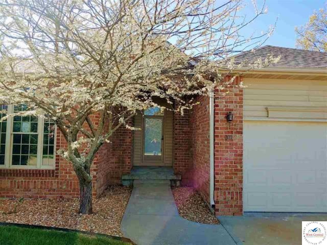 entrance to property with a garage, brick siding, and a shingled roof