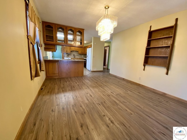 kitchen featuring brown cabinets, decorative backsplash, glass insert cabinets, wood finished floors, and a peninsula