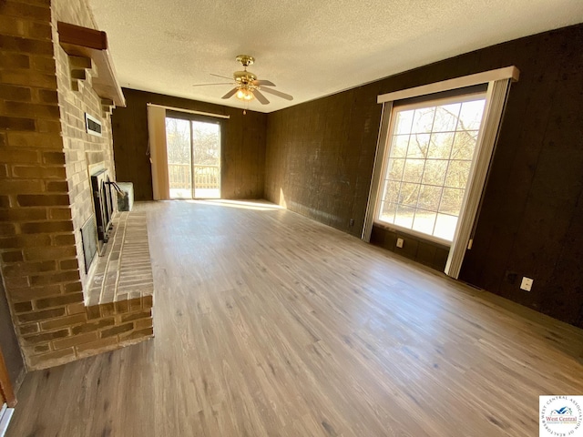 unfurnished living room with a ceiling fan, a fireplace, a textured ceiling, and wood finished floors